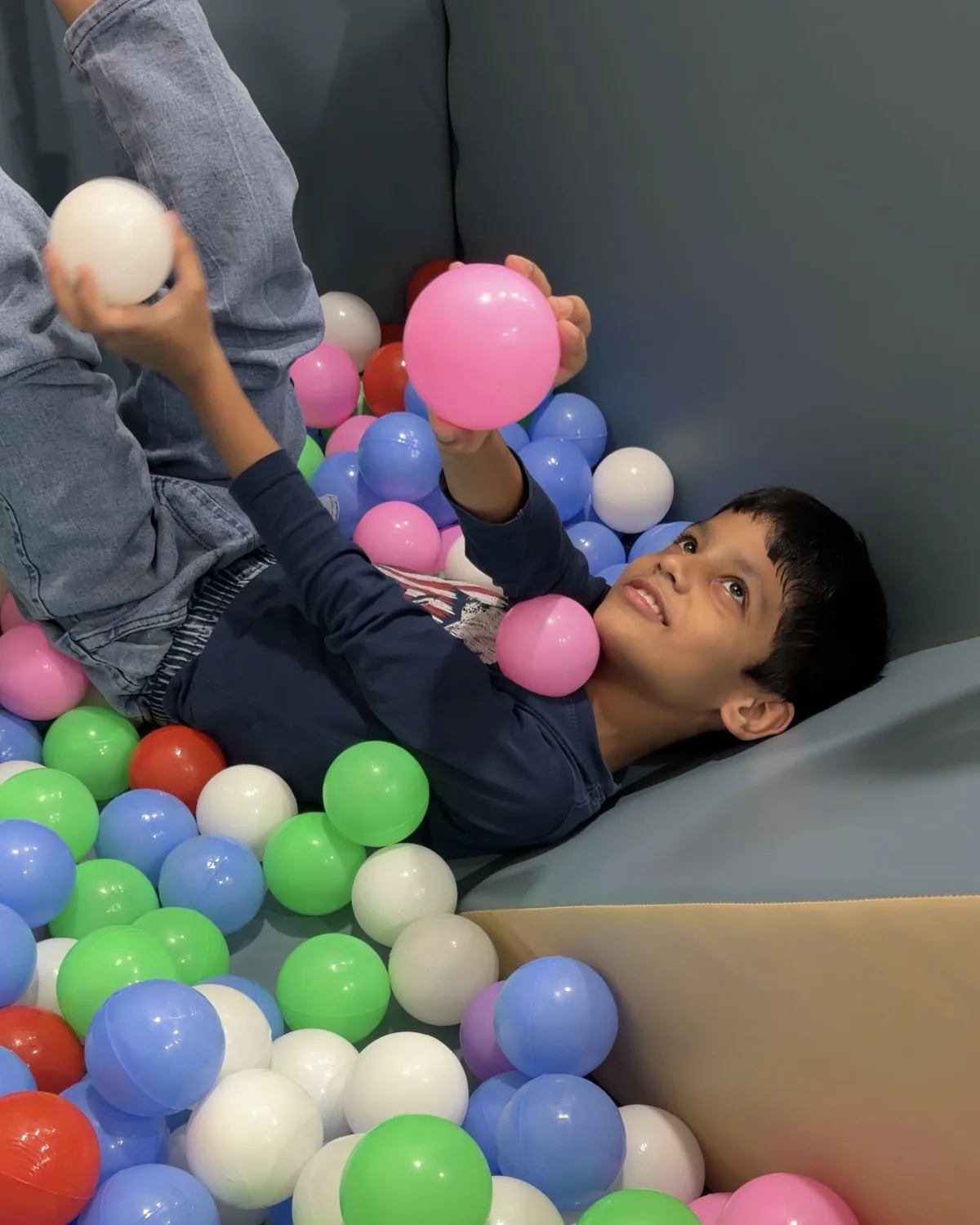A boy laughing in the ball pit at Devine