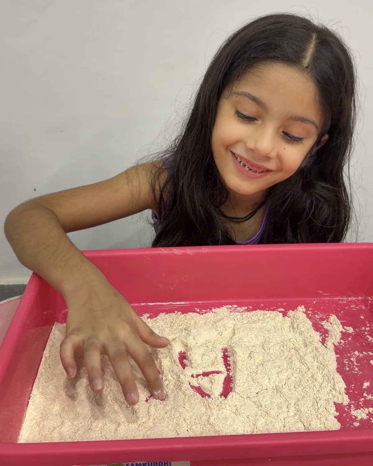 A girl smiling while playing in a sensory sand tray at Devine